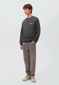 Felpa grigia scura con scollo a girocollo e dettagli del logo bianco, abbinata a jeans grigi larghi e sneaker di colore chiaro.