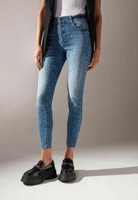 Högmidjade blå denimjeans med en blekt design, femknappsstängning och slim fit, i kombination med svarta plattformsskor.