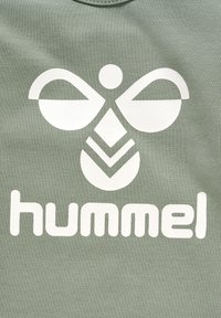 Grøn bomulds t-shirt med et stort hvidt logo med symmetriske former, herunder et sommerfugl symbol og ordet "hummel" nedenfor.