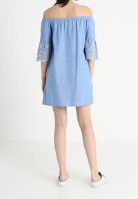 Light blue off-the-shoulder dress with lace-trimmed bell sleeves, made of soft fabric. Short length and relaxed fit, paired with white sneakers.