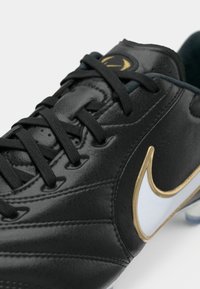 Μαύρο αθλητικό παπούτσι με λείο δερμάτινο φινίρισμα, με μαύρα κορδόνια, χρυσό λογότυπο Nike και λευκή λεπτομέρεια σβούρας.