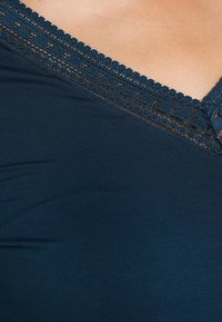 Haut bleu marine avec un design à col en V, présentant une délicate finition en dentelle le long du col et une texture de tissu lisse.