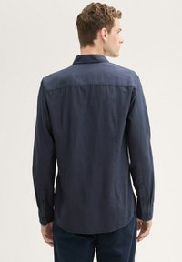 Camisa de manga larga azul marino hecha de tejido ligero, con un corte recto, puños abotonados y un cuello clásico con una textura suave.