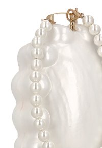 Bílý perlový náhrdelník se zlatou sponou, s jednotnými kuličkami, lesklým povrchem a uspořádaný v symetrickém vzoru.