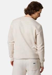 Light beige sweatshirt with a crew neck, ribbed cuffs, and hem. Soft fabric texture with a patch on the lower back of matching sweatpants.