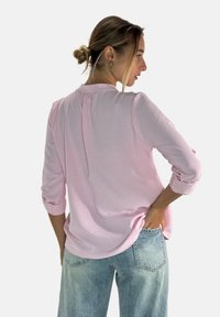 Jasnoróżowa koszula z długim rękawem o luźnym kroju, z detalem fałdy z tyłu i podwiniętymi mankietami, w zestawie z jasnoniebieskimi dżinsami.