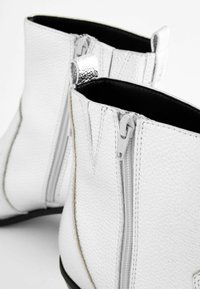 Las botas de tobillo de cuero blanco cuentan con un acabado texturizado, cremalleras laterales y un interior negro. Suela lisa con detalles de costura mínimos.