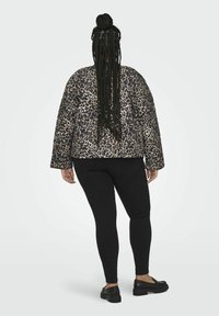 Pledinė leopardo rašto striukė bežėje ir juodoje spalvose, su laisvu kirpimu ir ilgomis rankovėmis, derinama su juodais siaurais džinsais ir juodais batais.
