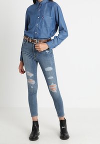Blue denim button-up shirt with a chest pocket, worn with light blue ripped skinny jeans and black ankle boots, accented by a leopard print belt.