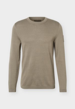 Maglione beige a maniche lunghe con scollo tondo in maglia, con polsini e orlo a coste, caratterizzato da un piccolo dettaglio a toppa sulla parte superiore della manica sinistra.