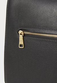 Sac en cuir noir avec une fermeture éclair dorée dotée d'un tirant et d'une couture contrastante le long de la poche zippée, texture mate.