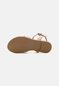 Sandalo beige con suola in gomma testurizzata. Presenta una cinghia alla caviglia regolabile e una base della punta ampia, una tomaia in materiale sintetico liscio e un design minimalista.