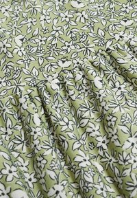 Tissu vert avec un motif floral en blanc et noir, présentant de petites fleurs et des feuilles. Texturé avec des plis doux pour un détail supplémentaire.