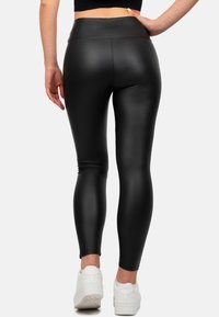 Leggings neri a vita alta realizzati in materiale liscio ed elasticizzato, design aderente, gambe affusolate e abbinati a scarpe da ginnastica bianche.