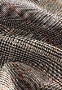 Woven fabric featuring a checkered pattern in black, brown, and beige tones, with varied textures and diagonal lines throughout.
