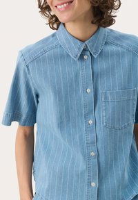 Denimhemd in Hellblau mit weißen vertikalen Streifen. Kurze Ärmel, Knopfleiste vorne und eine Brusttasche. Glatte Textur.