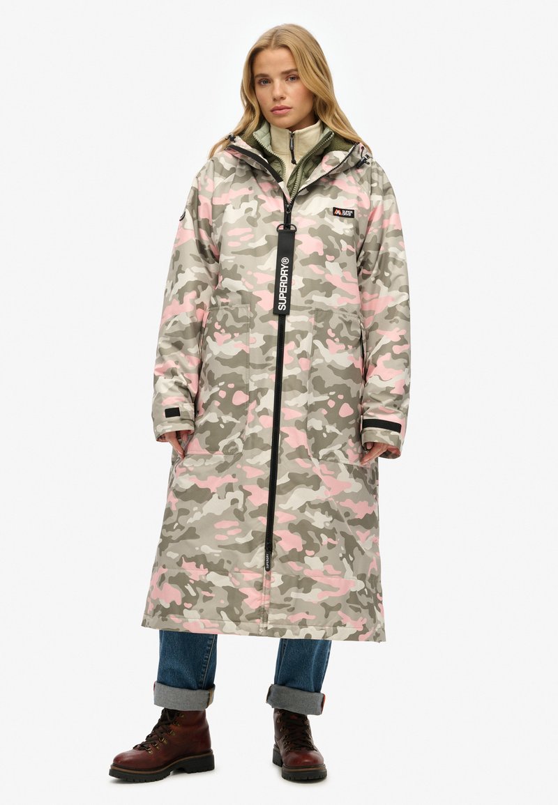 Parka camouflage dans des tons gris, rose et vert atténués ; elle dispose d'une fermeture éclair complète, d'une capuche, de grandes poches et d'accents en métal noir.