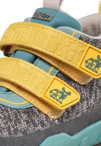 Sneaker in tessuto grigio con cinturini in Velcro gialli, accenti turchesi, rete testurizzata e suola in gomma. Presenta una grafica di un animale blu sul cinturino.