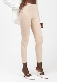 Beige, nauwsluitende broek met zijknopen, een soepele textuur en een hoge taille. Gecombineerd met witte slingback hakken met een puntige neus.