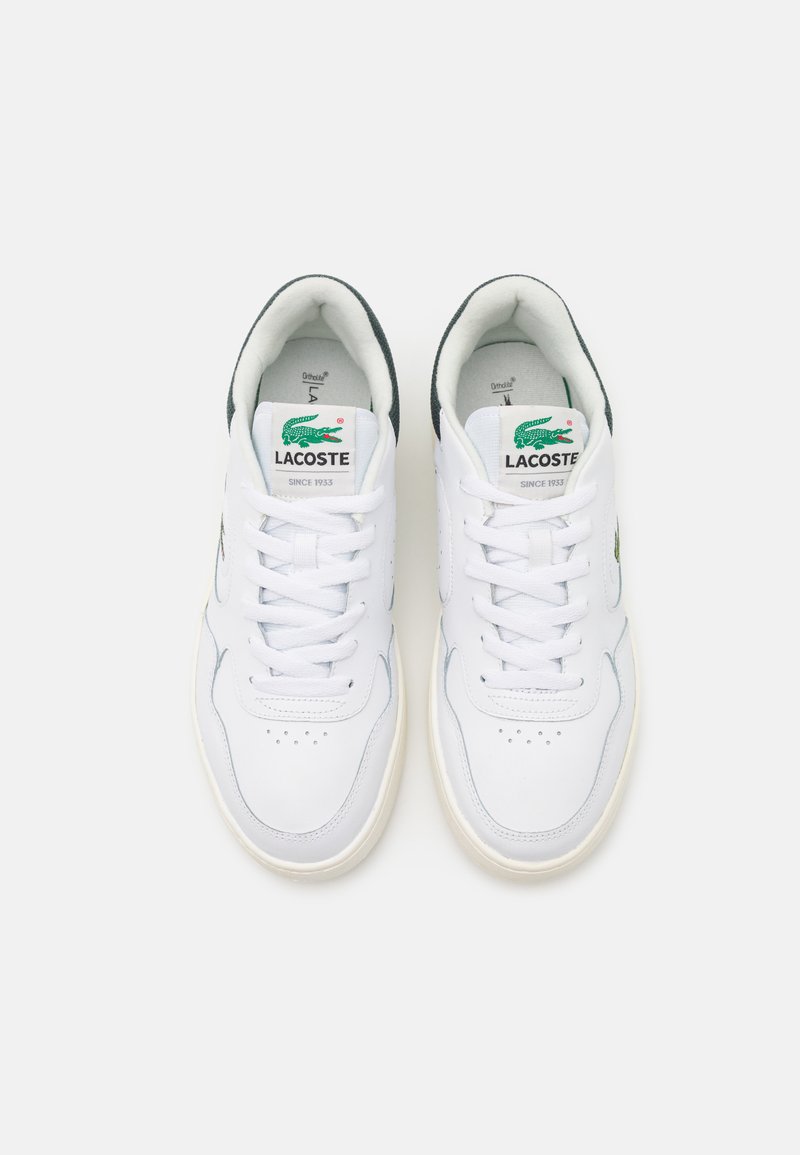Sneakers bianchi in pelle con una texture liscia, caratterizzati da un logo Lacoste verde, punta rotonda e design classico con lacci.