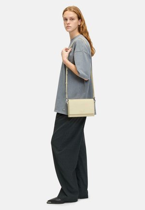 Gray oversized shirt, black wide-leg pants, and a light yellow crossbody bag with a simple design and adjustable strap. Smooth textures.