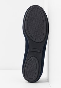 Chaussure de promenade en daim marine à enfiler avec une semelle en caoutchouc noir. La semelle présente un motif texturé et une étiquette de marque subtile.