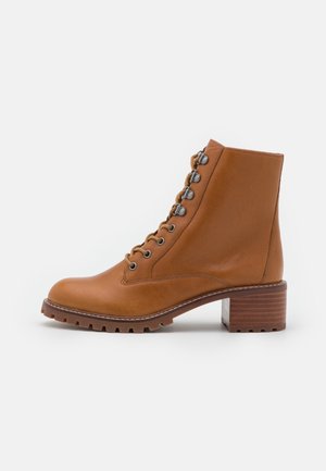 Bottes chelsea en cuir tan avec un bout rond, un laçage à l'avant et des détails en métal argenté, présentant un talon bloc texturé haut et une semelle robuste.