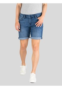 Denim shorts in medium blue met opgerolde boorden, voorzien van een klassiek vijf-pocket ontwerp en een knoopsluiting. Gemaakt met witte sneakers.