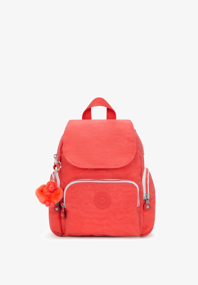 Mochila color coral con una textura suave, forma redondeada, cierre con solapa, cremalleras blancas contrastantes y un llavero en forma de mono.