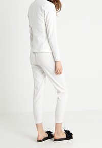 Blazer bianco a righe sottili e pantaloni fitted coordinati, abbinati a sandali neri con dettaglio a fiocco e suola bianca. Materiale liscio.