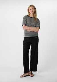Gehaakte zwart-wit gestreepte top met korte mouwen, gecombineerd met losse zwarte broek en zwarte sandalen met bandjes. Effen achtergrond.
