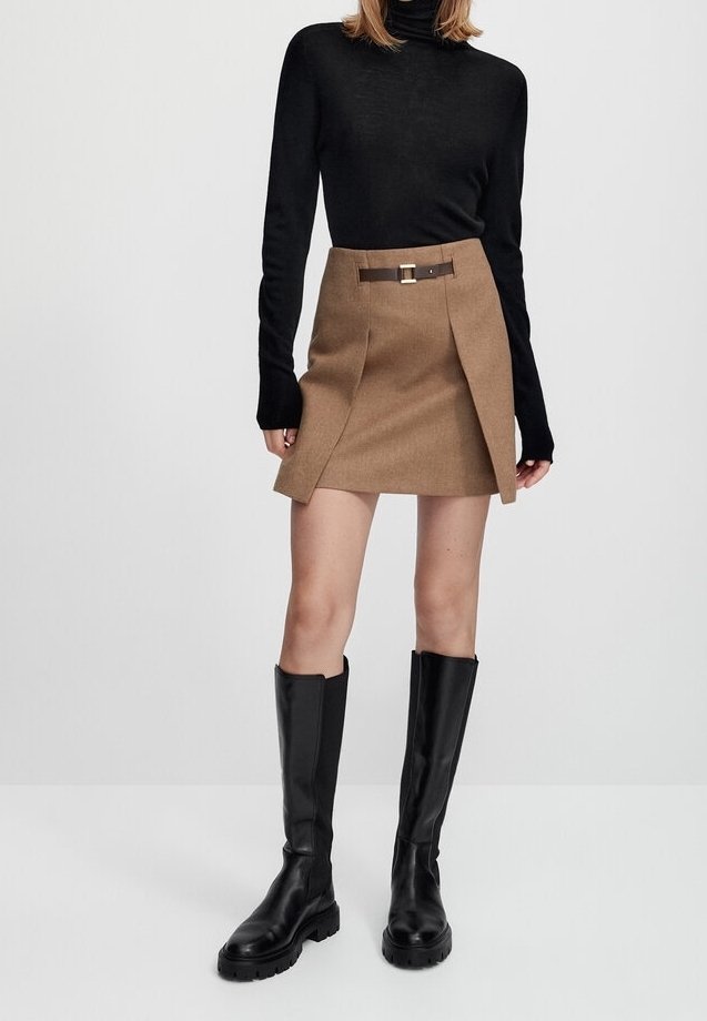 Zwarte turtle neck, bruine minirok met zijplooien en ceintuurbeslag, gecombineerd met kniehoge zwarte leren laarzen. Soepele stoftextuur.