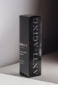 Czarna pudełkowa opakowanie dla serum przeciwstarzeniowego; charakteryzuje się wyraźnym białym tekstem, błyszczącym wykończeniem oraz zawiera informacje o marce i produkcie w minimalistycznym designie.