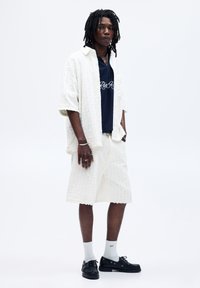 Hvid tekstureret kortærmet skjorte og matchende shorts, parret med en marineblå t-shirt og sorte sko, med en afslappet pasform og casual design.