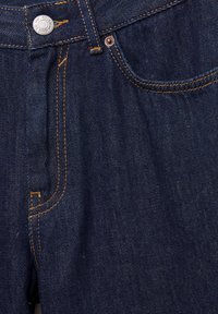 Tamno plave traperice s narančastim šavovima, prednjim zatvaračem na gumbe i dva džepa. Materijal izgleda čvrsto s blagim sjajem.