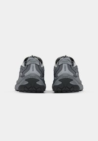 Pantofi sport gri cu un cap superior texturat, talpă moale, accente reflectorizante și o formă rotundă, concepuți pentru confort și susținere.