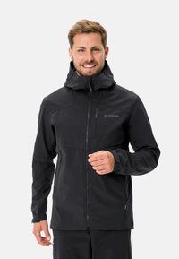 Giacca softshell nera con zip frontale, cappuccio regolabile e tasche. Presenta una texture liscia e un design minimal con accenti sottili.
