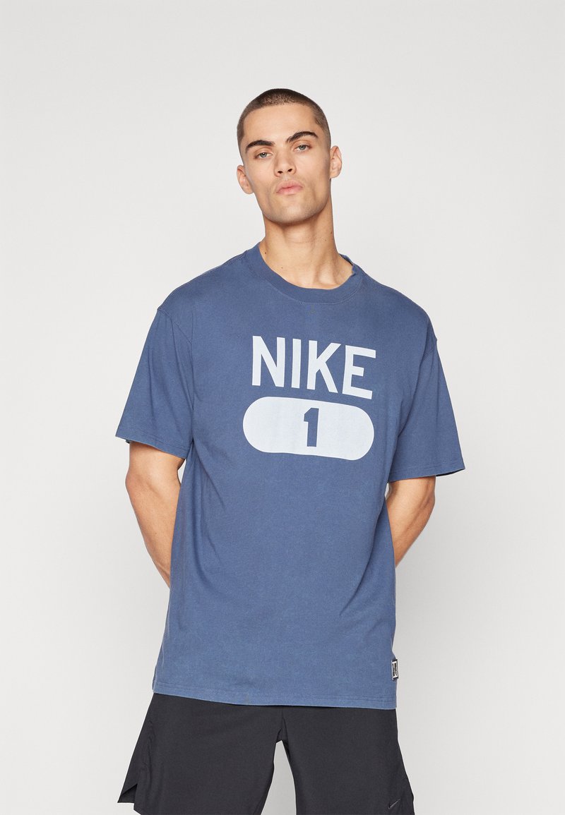 Blå bomulds t-shirt med et stort hvidt "NIKE" logo og "1" grafisk motiv på fronten, med en afslappet pasform og korte ærmer.