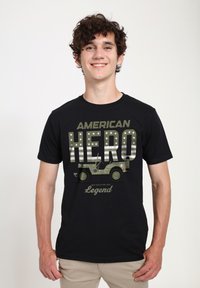 Camiseta de algodón negra con el texto "HÉROE AMERICANO" en negrita verde, una gráfica de un Jeep Willys de 1944 y estrellas.