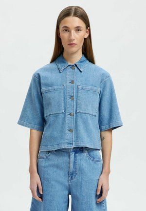 Ljusblå denimjacka med korta ärmar, två framfickor, knäppning med knappar och rå kant. Bärs tillsammans med matchande blå denimshorts.