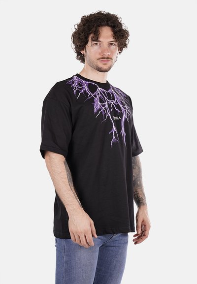 T-shirt in cotone nero con grafica di fulmini viola sul petto, colletto tondo e maniche corte. Il modello indossa jeans slim-fit blu.