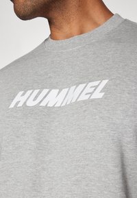 Grijze katoenen t-shirt met een ronde halslijn, met een opvallend wit "HUMMEL" logo in een schuine lettertype over de borst.