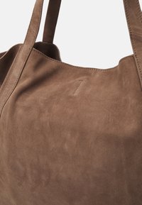 Borsa a tote in suede marrone con una texture morbida e apertura superiore. Presenta manici piatti e robusti e cuciture minime. Senza hardware o dettagli visibili.