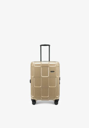 Valise rigide dorée avec quatre roues noires pivotantes et une poignée télescopique noire déployée en position verticale.