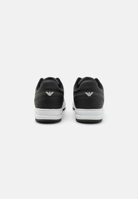 Sneaker in pelle nera con colletto imbottito, suola intermedia bianca e dettagli testurizzati. Presenta un logo argento sul tallone.