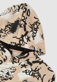 Felpa con cappuccio in tessuto beige caratterizzata da stampe in stile graffiti nero e bianco. Texture morbida con una fodera interna nera nel cappuccio.