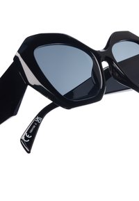 Mustikka ylisuuret aurinkolasit rohkealla geometrisellä kehysrakenteella, tummansävyisillä linsseillä ja kiiltävällä pinnalla. Varret on muotoiltu kulmikkaiksi ja niissä on painetut yksityiskohdat.