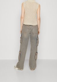 Beige gestricktes ärmelloses Top, kombiniert mit lockeren, verwaschenen Cargo-Hosen mit mehreren Seitentaschen und einem lässigen Schnitt.