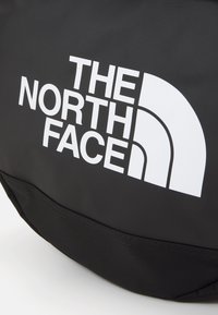 Zwarte tas met een opvallend wit logo van The North Face. Het materiaal lijkt textuur te hebben, met een duurzaam ontwerp en een eenduidig kleurenpalet.