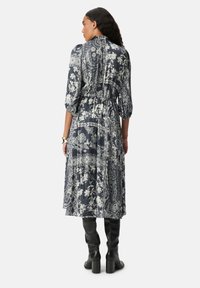 Lungo vestito blu navy con motivi floreali e paisley bianchi, dotato di maniche puff, vita arricciata e orlo fluente, abbinato a stivali neri al ginocchio.